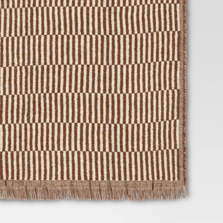 A brown and cream colored striped blanket with fringed edges.
