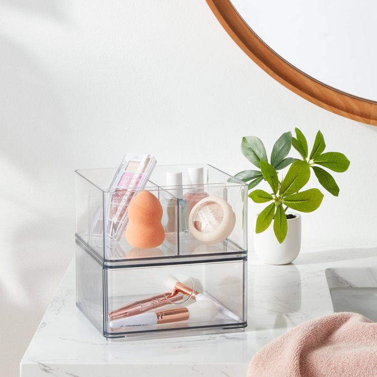 Clear acrylic storage organizer with two compartments holding makeup items on a marble countertop.
