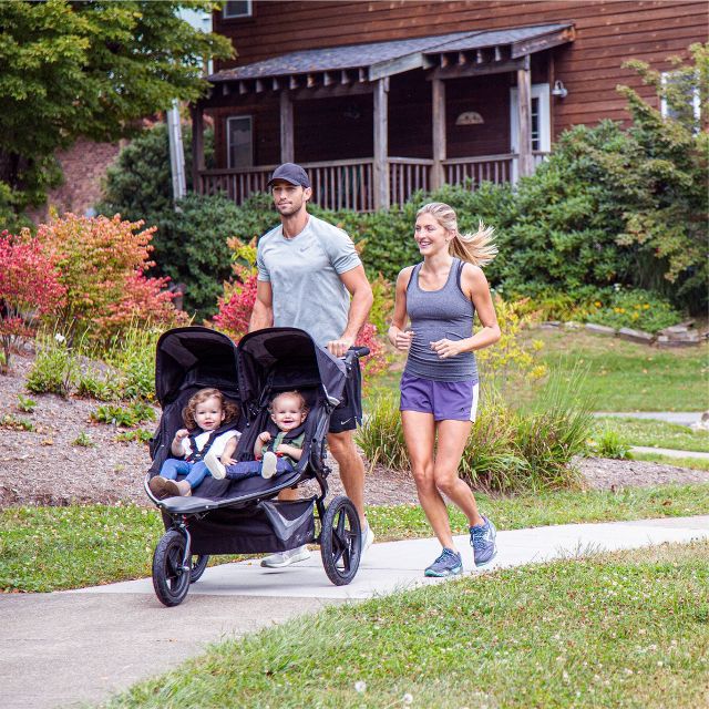 Parent pushing a baby stroller with canopy on a walk.