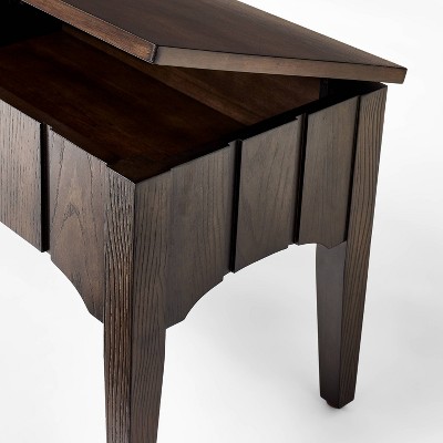Detail of the top and front paneling of a dark wood storage ottoman.