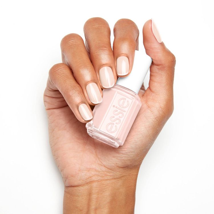 A hand holding a bottle of light pink colored nail polish with matching painted nails.