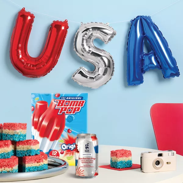 USA balloon in red, silver and blue. Over a table with red, white and blue rice treats. Along with bomb pops popsicles and a rocket pop good & gather flavored water.