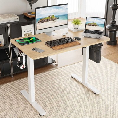 Desk in a home office setup with large monitor, laptop, and keyboard on wooden desk