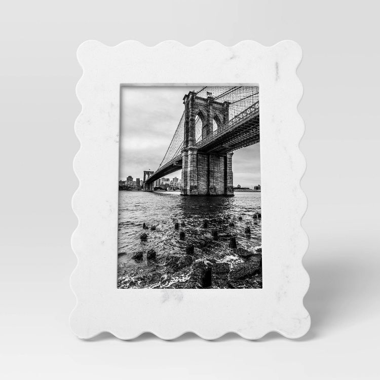 A white colored frame with a wavy edge design holds a black and white photograph of a bridge over water.