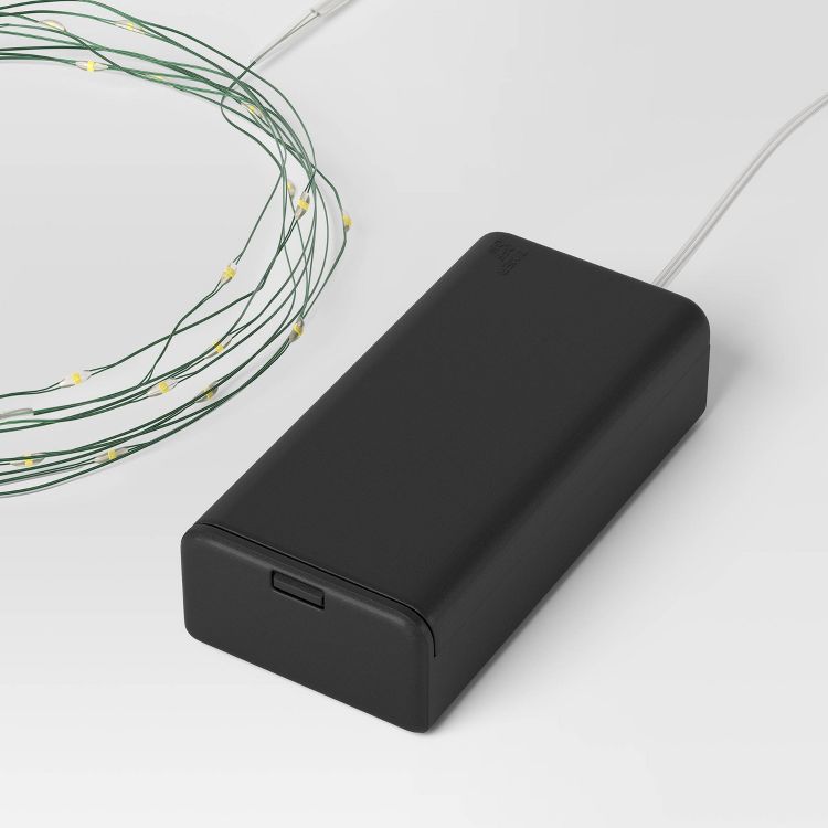 A coil of string lights with small yellow colored bulbs connected to a black rectangular battery pack.
