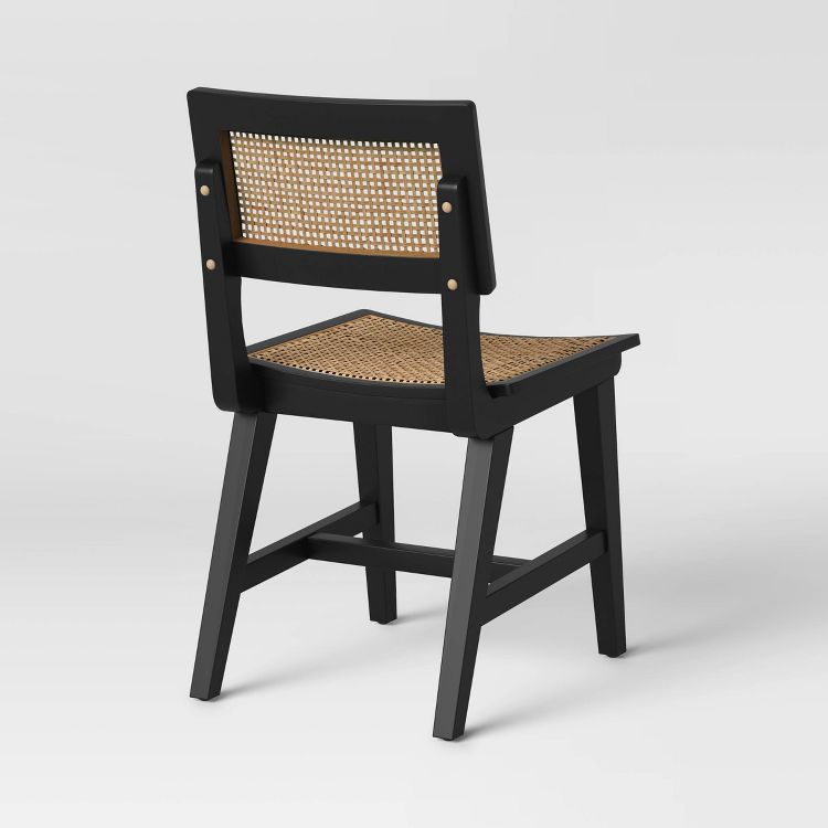 A black colored dining chair with a woven rattan backrest and seat.