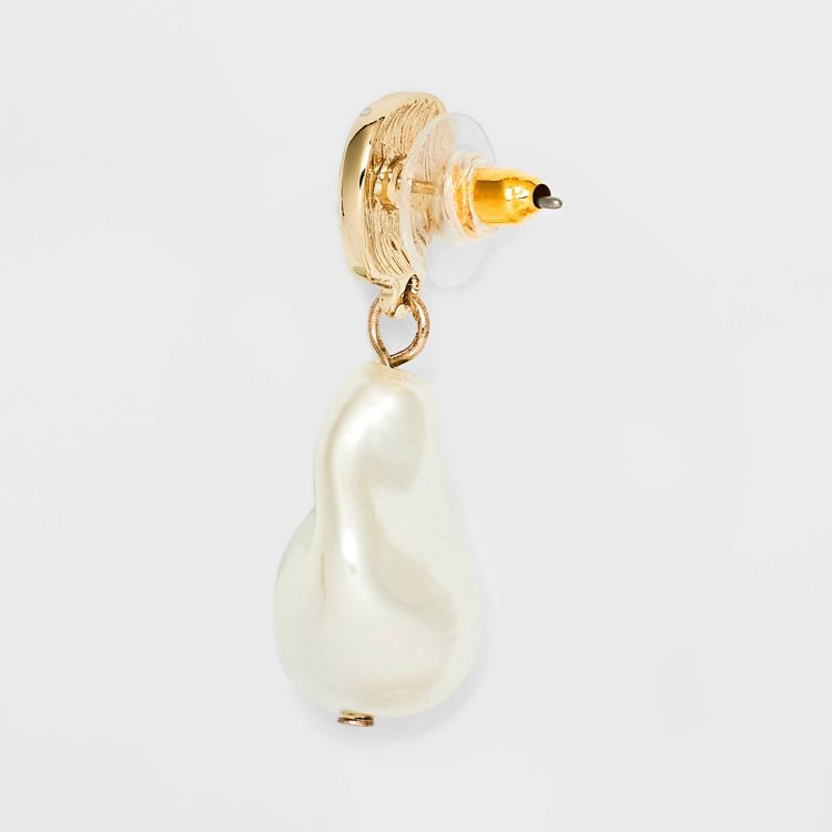 A gold colored stud earring with a dangling white pearl-like drop.