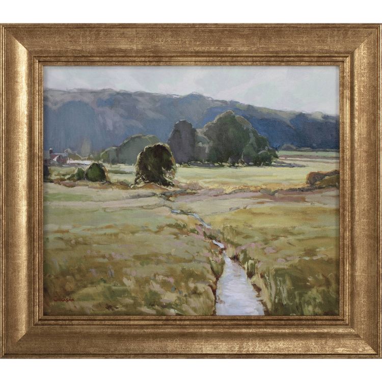 A framed landscape painting depicting a serene field with a small stream, trees, and distant hills under a soft sky.