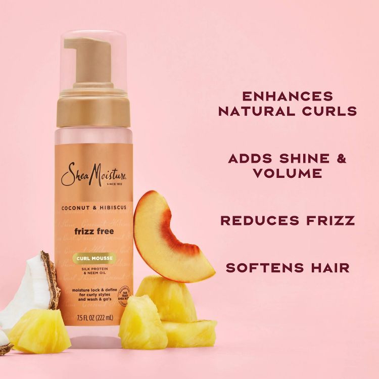 A bottle of SheaMoisture Coconut & Hibiscus Curl Mousse with text highlighting benefits like enhancing natural curls, adding shine and volume, reducing frizz, and softening hair, surrounded by coconut and pineapple pieces.