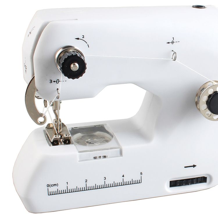 White sewing machine with visible thread path, tension dials, and a ruler marked in centimeters on the base.