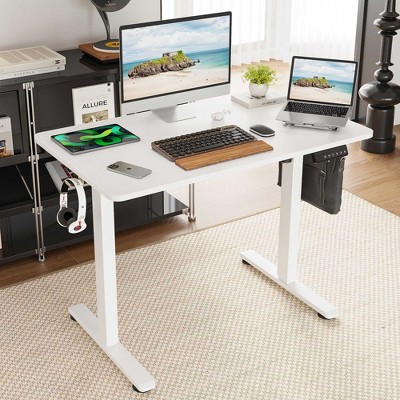 White standing desk in a cozy home office with multiple devices and a bag