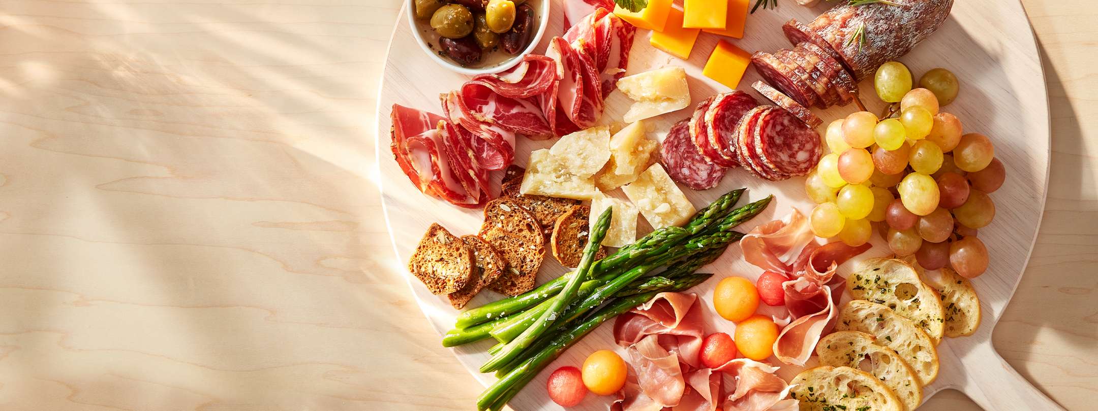 An appetizing charcuterie board with various cheeses, cured meats, olives, grapes, and asparagus on a wooden surface.