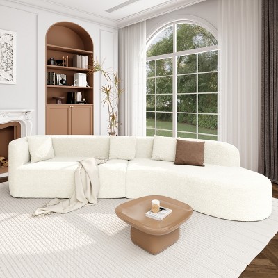 Cream curved sectional sofa with brown pillow and small table in living room