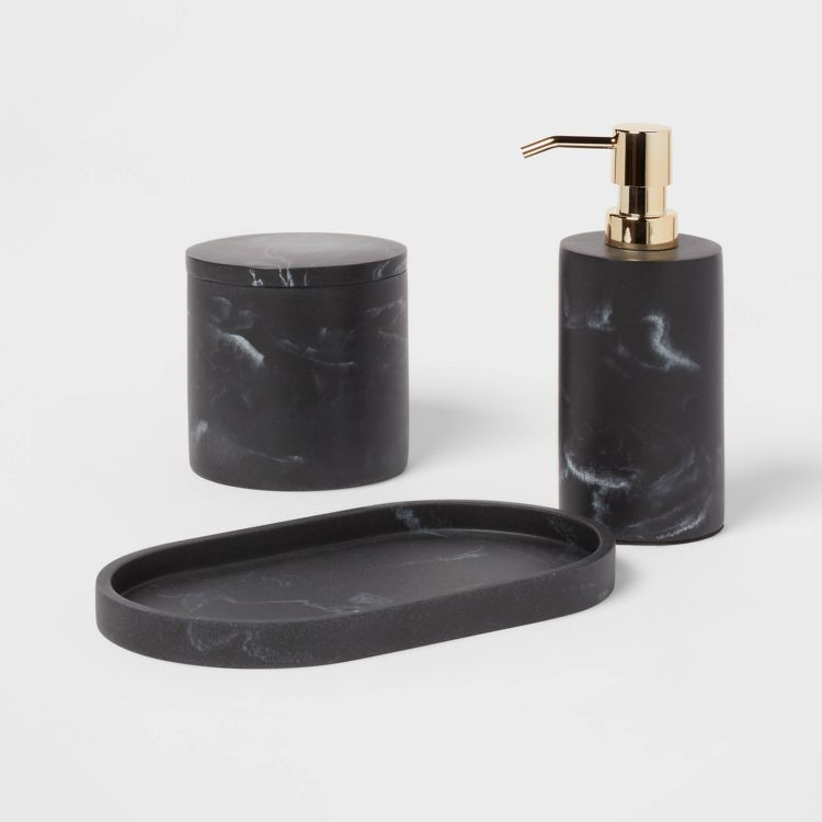 A black colored oval tray with a marbled pattern is placed in front of a matching cylindrical container and a soap dispenser with a gold colored pump.
