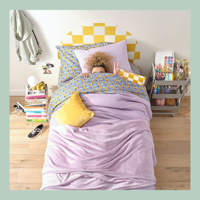 Girl covered with purple bed sheets peeking and giving the frame a peace sign. 