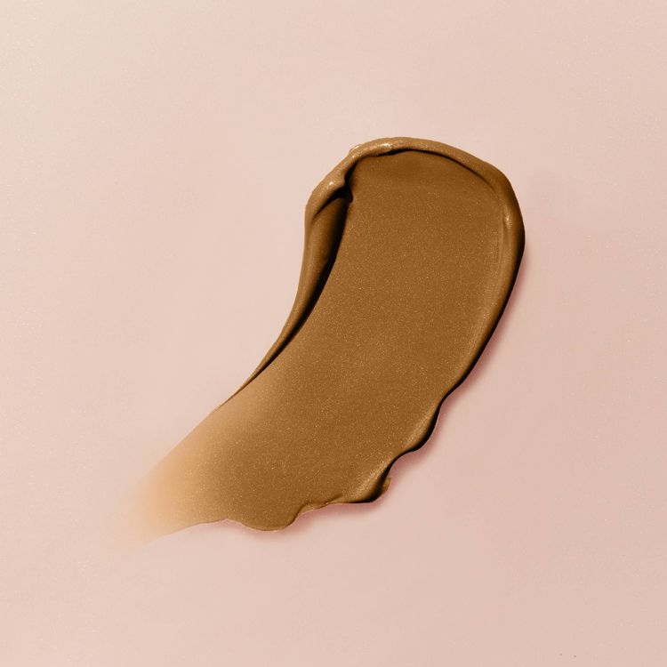 A swatch of shimmery bronze colored highlighter on a light pink background.
