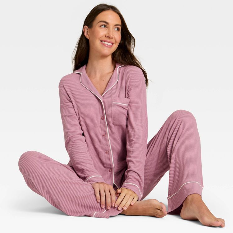 Pink colored pajama set with white piping, featuring a long-sleeve button-up top and matching pants.