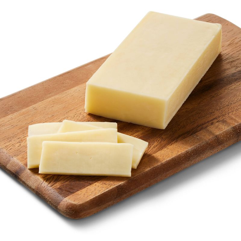 A block of pale yellow colored cheese with several slices cut, placed on a wooden cutting board.