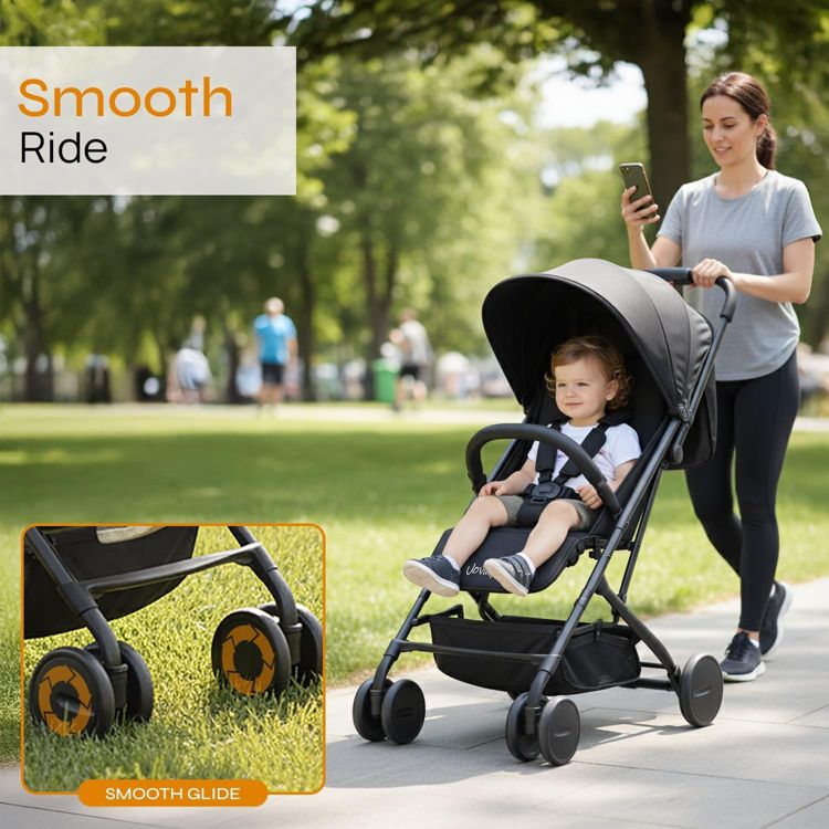 A black colored stroller with a canopy and smooth glide wheels, being pushed on a paved path.