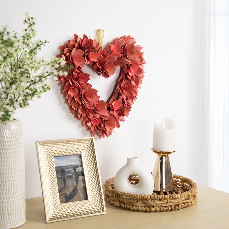 Heart-shaped wreath with red colored leaves hanging on a white wall above a table with decorative items.