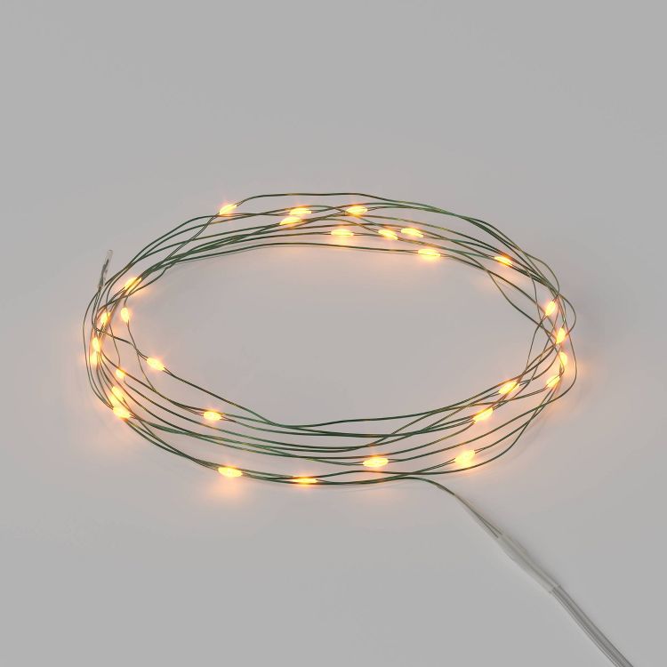 A coil of green wire string lights with warm yellow colored bulbs arranged in a circle.