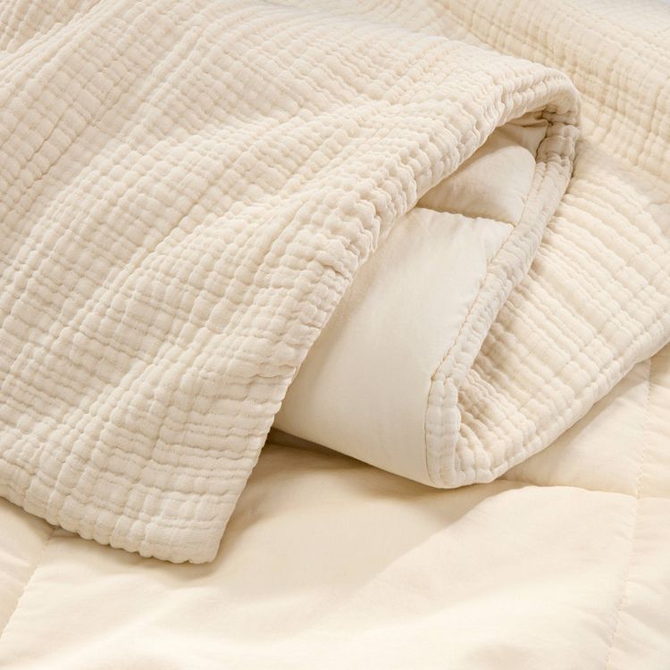 Textured chambray comforter in a natural color, partially folded to reveal a smooth inner lining.