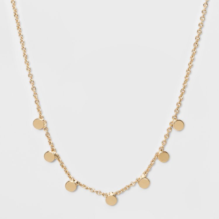 A gold colored necklace with small round disc charms evenly spaced along the chain.
