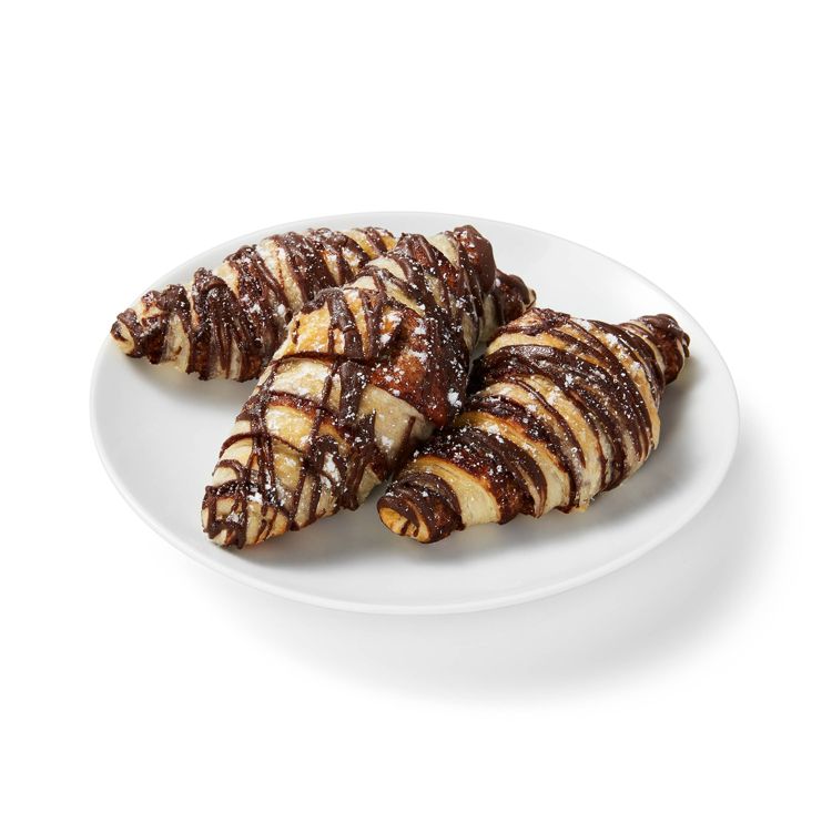Three croissants drizzled with chocolate and dusted with powdered sugar on a white plate.