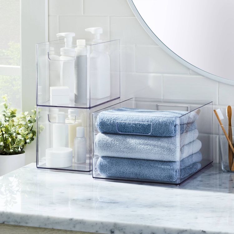 Clear plastic bathroom trays on a marble countertop hold white bottles and folded blue colored towels.