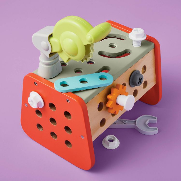 Colorful toy tool set with a wooden block, plastic gears, bolts, and a wrench on a purple surface.