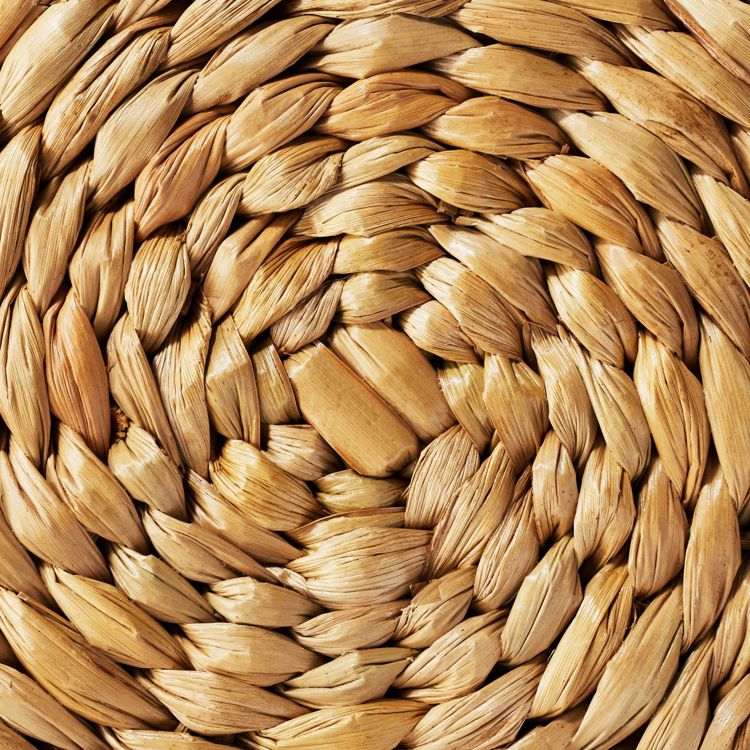 A close-up of a woven, natural-colored textured surface, likely part of an ottoman or bench.