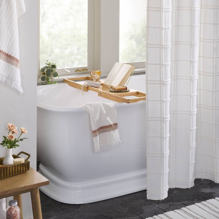 A wooden bath tray placed across a white bathtub, holding a book, a glass, and a soap dish.