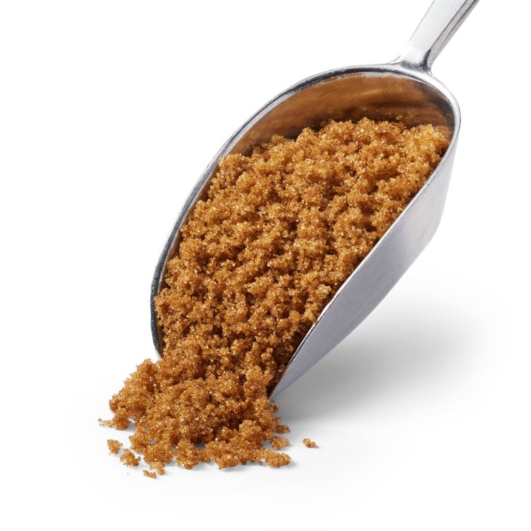A metal scoop filled with brown colored sugar spilling onto a white surface.
