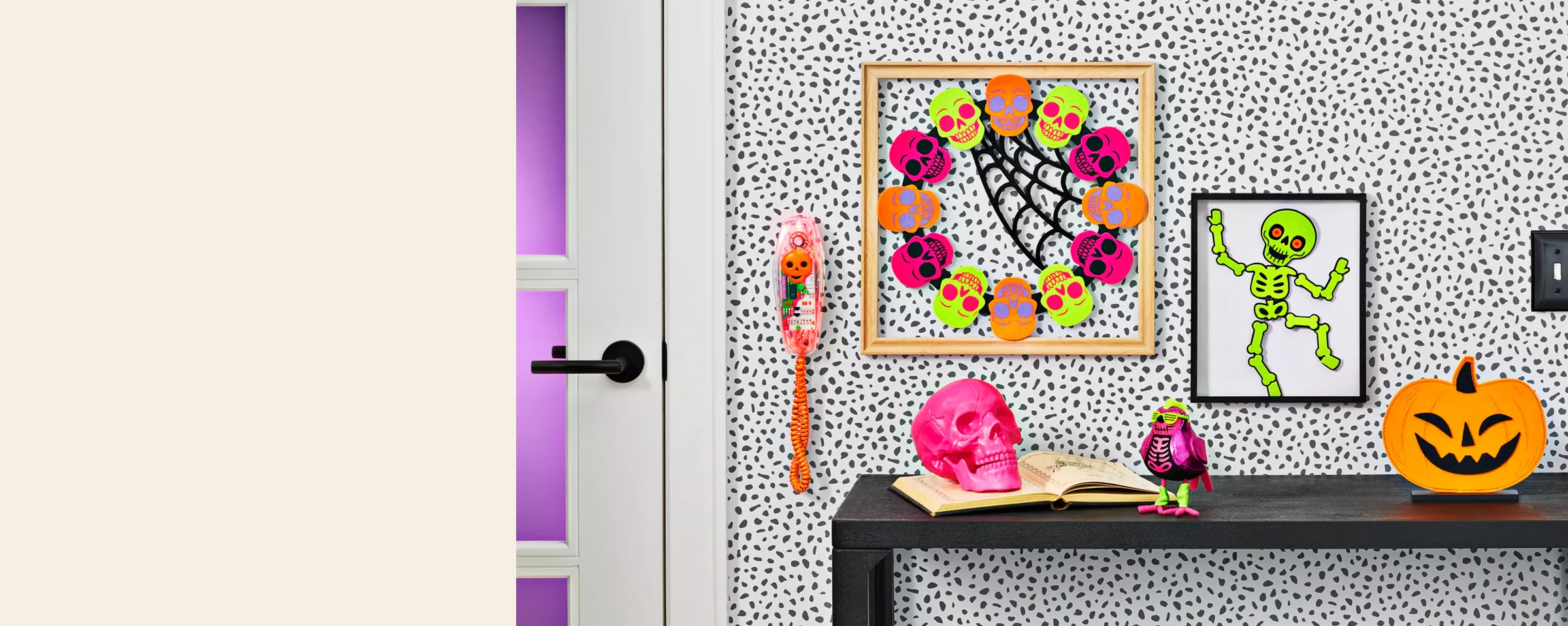 This decor is bright, fun & reflective of the 80s. A pumpkin, pink skull & small purple bird with neon green accessories sit on a side table. A wreath of multi-colored skulls hangs on the wall between a framed skeleton & a Halloween wall phone.