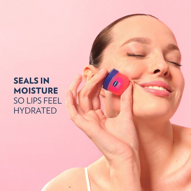 A person holds a small pink and blue colored lip balm container near their face, with the text "SEALS IN MOISTURE SO LIPS FEEL HYDRATED" visible.