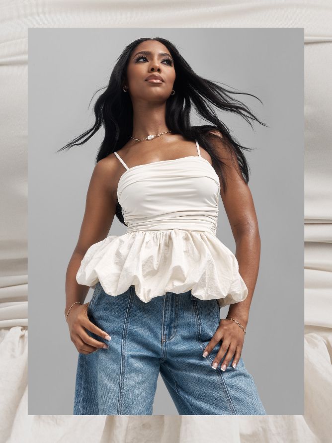 Tatiana Elizabeth sports light-wash 90s baggy jeans with a white tank blouse that's fitted on the top and flows out at the waist with fluffy texture. Simple metallic jewelry completes her look.