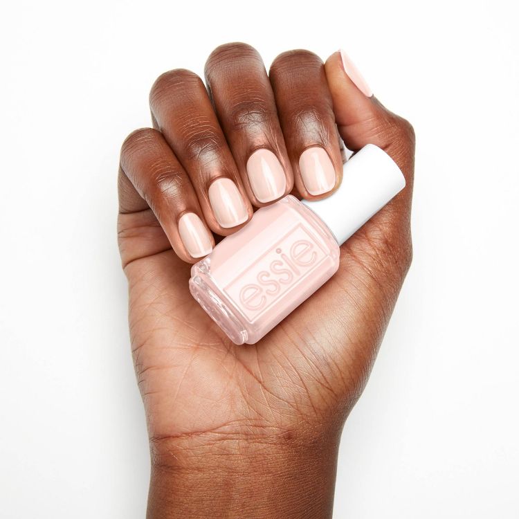 A hand holding a bottle of light pink colored nail polish with the brand name "essie" on the bottle, and nails painted in the same shade.
