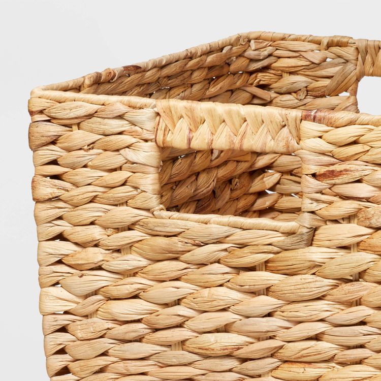 A woven natural colored basket with a rectangular cutout handle.