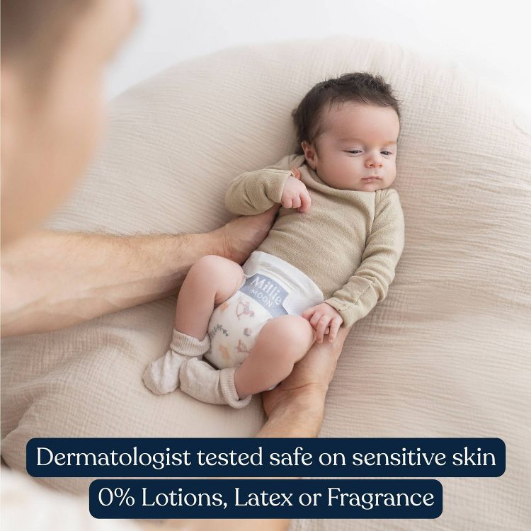 A baby wearing a diaper with "Millie Moon" text, held by an adult, with text stating "Dermatologist tested safe on sensitive skin, 0% Lotions, Latex or Fragrance."