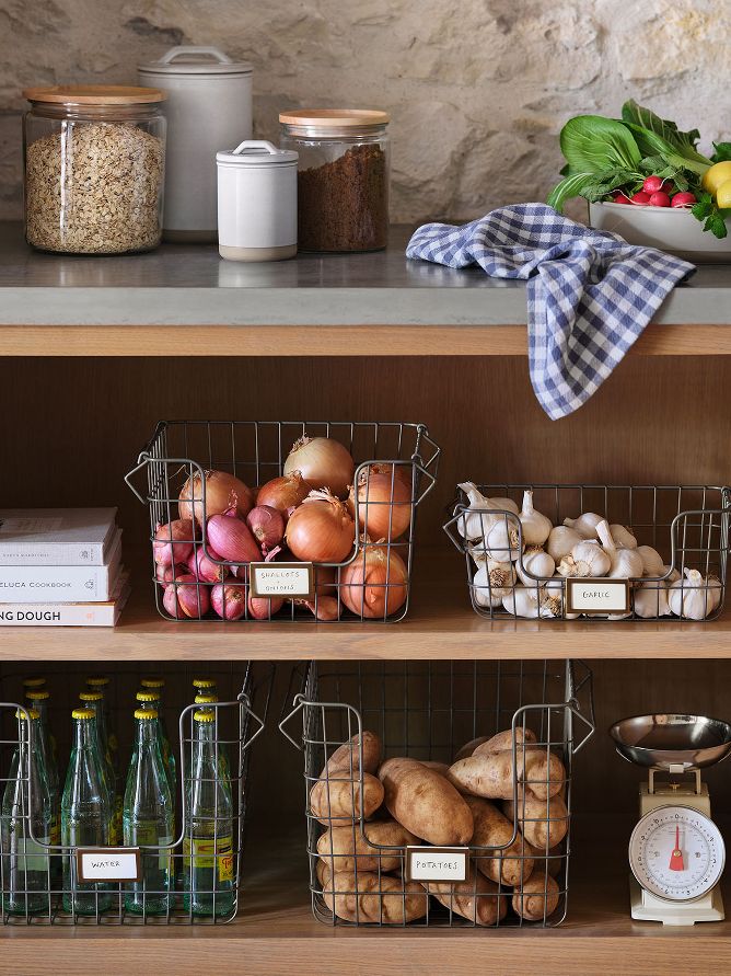 Kitchen shelfs with produce in wired baskets. Various jars on counter top.