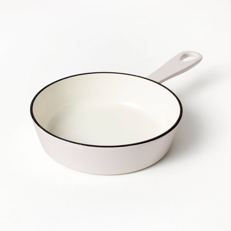 A light pink colored skillet with a white interior and a handle featuring a hole for hanging.