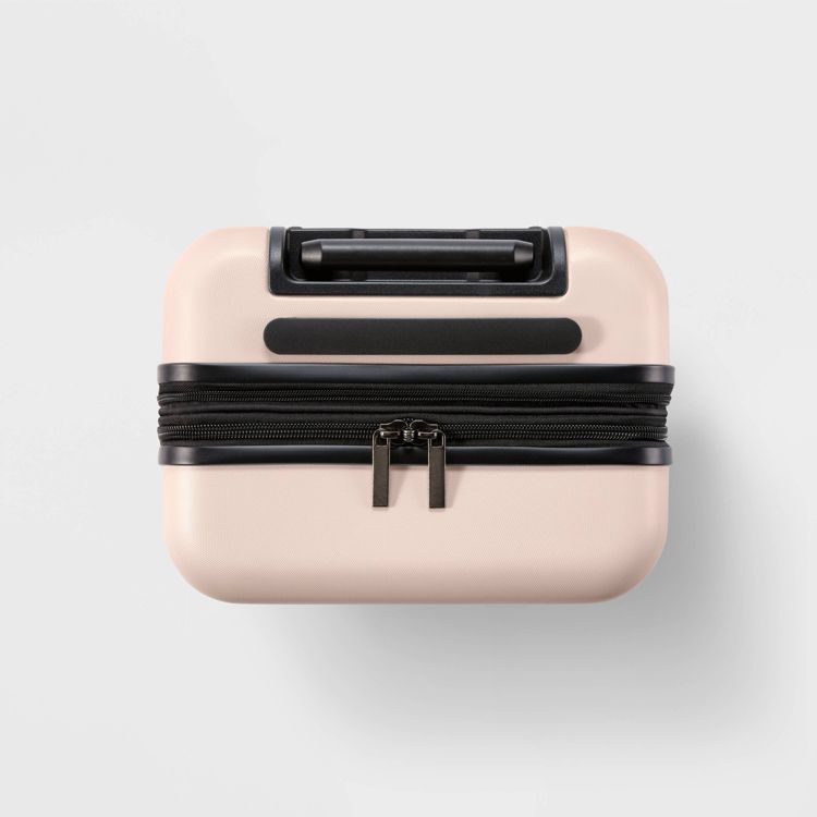 A small, light pink colored suitcase with a black handle and zipper, viewed from above.