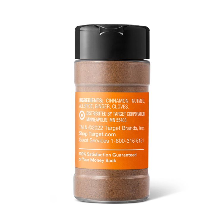 A clear plastic spice jar with a black lid and an orange label listing ingredients: cinnamon, nutmeg, allspice, ginger, and cloves.