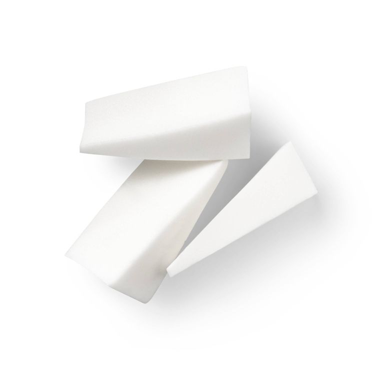 Three white colored triangular makeup sponges arranged on a white surface.