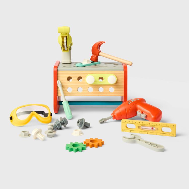 A colorful toy tool set featuring a wooden workbench, plastic hammer, screwdriver, drill, ruler, goggles, and various nuts and bolts.
