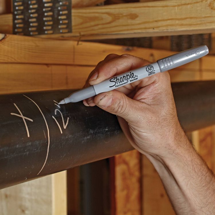 A hand holding a gray colored Sharpie permanent marker writing on a black pipe.