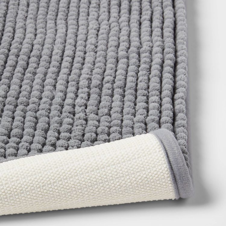 A gray colored textured bath mat with a white underside is partially rolled up.