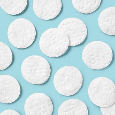 White cotton pads with a quilted texture scattered on a light blue colored background.