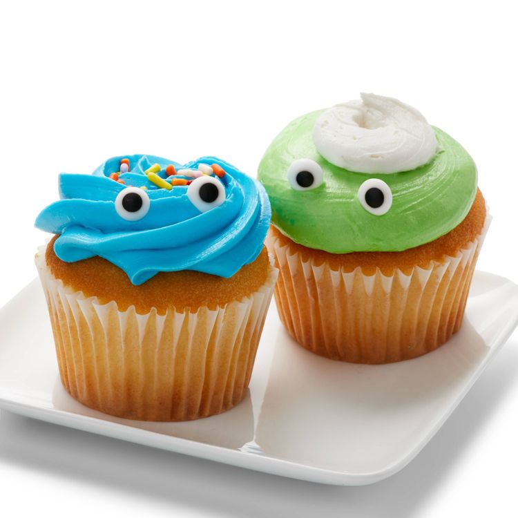 Two cupcakes with blue and green colored frosting, decorated with candy eyes and sprinkles, placed on a white plate.