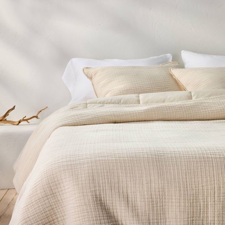 Natural-colored textured chambray comforter and sham set on a bed with white pillows, against a light wall.